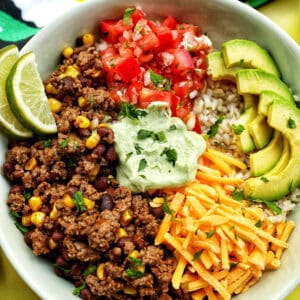 taco bowl with ground beef, beans, cheese, pico de gallo, avocado, rice, avocado cilantro lime crema.