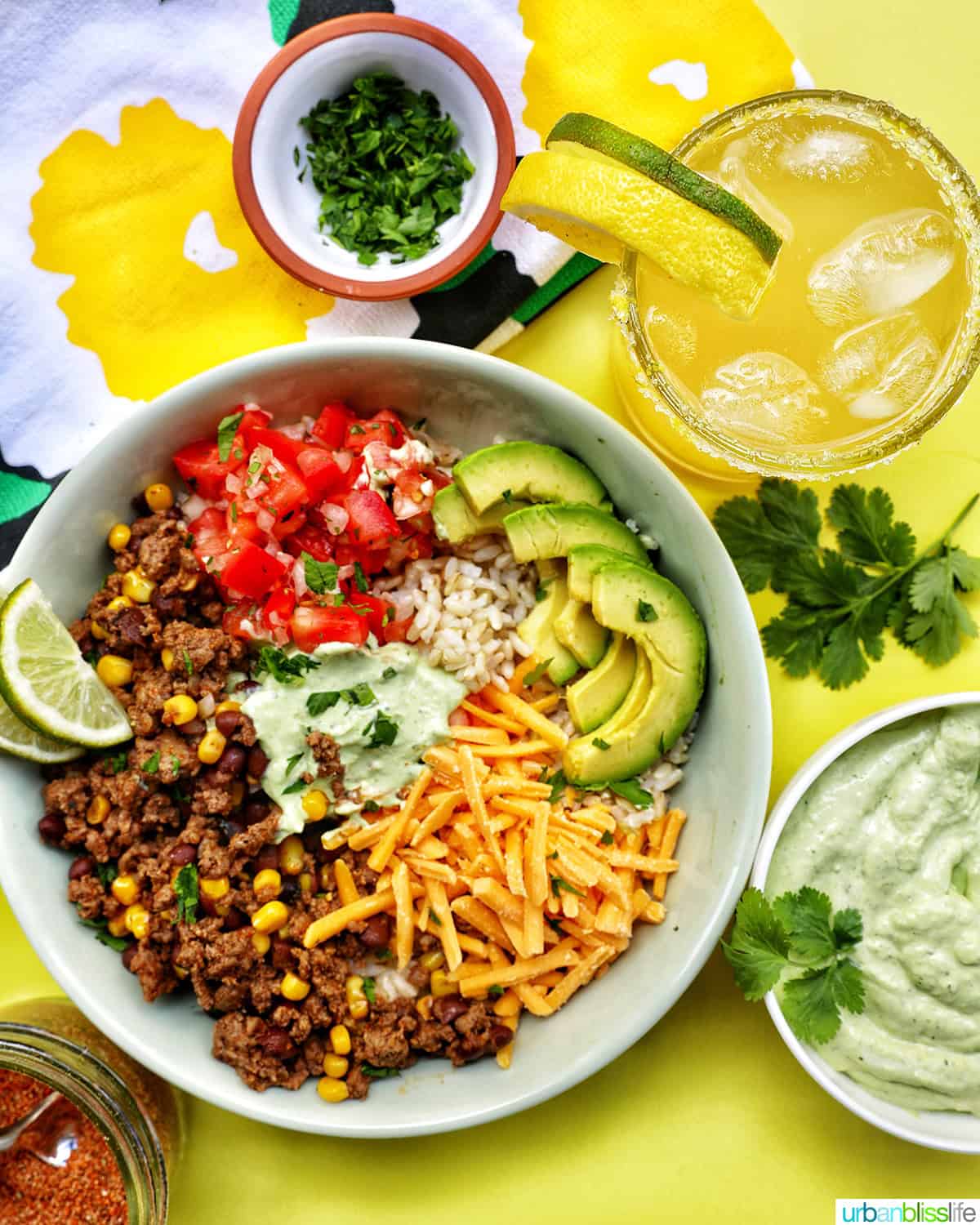 taco bowl with ground beef, beans, cheese, pico de gallo, avocado, rice, avocado cilantro lime crema with a yuzu margarita.