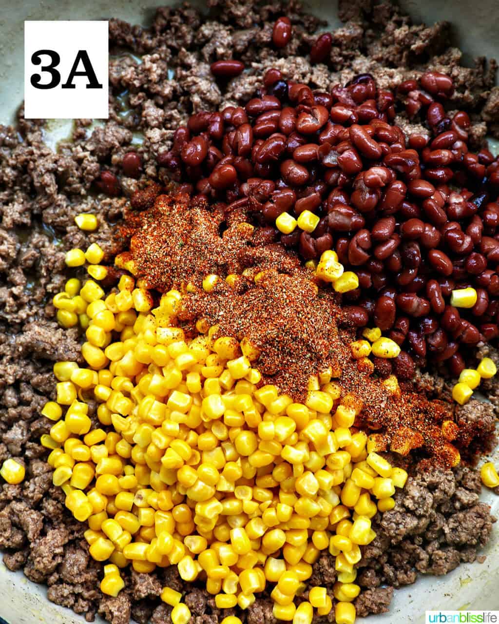 corn, seasonings, and beans added to cooked ground beef in a pan.