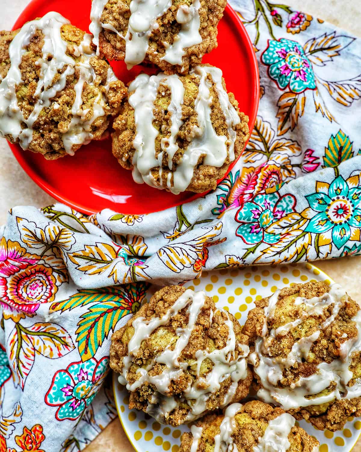 vegan streusel muffins with glaze on two plates and a colorful floral napkin.