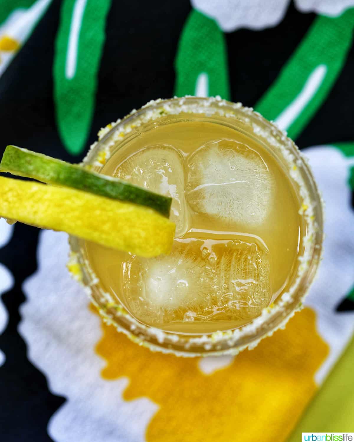 glass of yuzu margarita with slices of lemon and lime on brightly colored napkins.