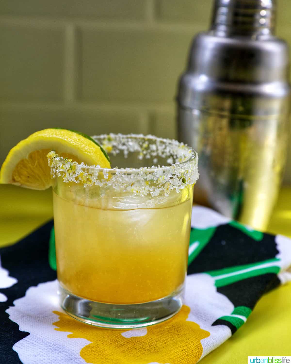 glass of yuzu margarita with slices of lemon and lime on brightly colored napkins.