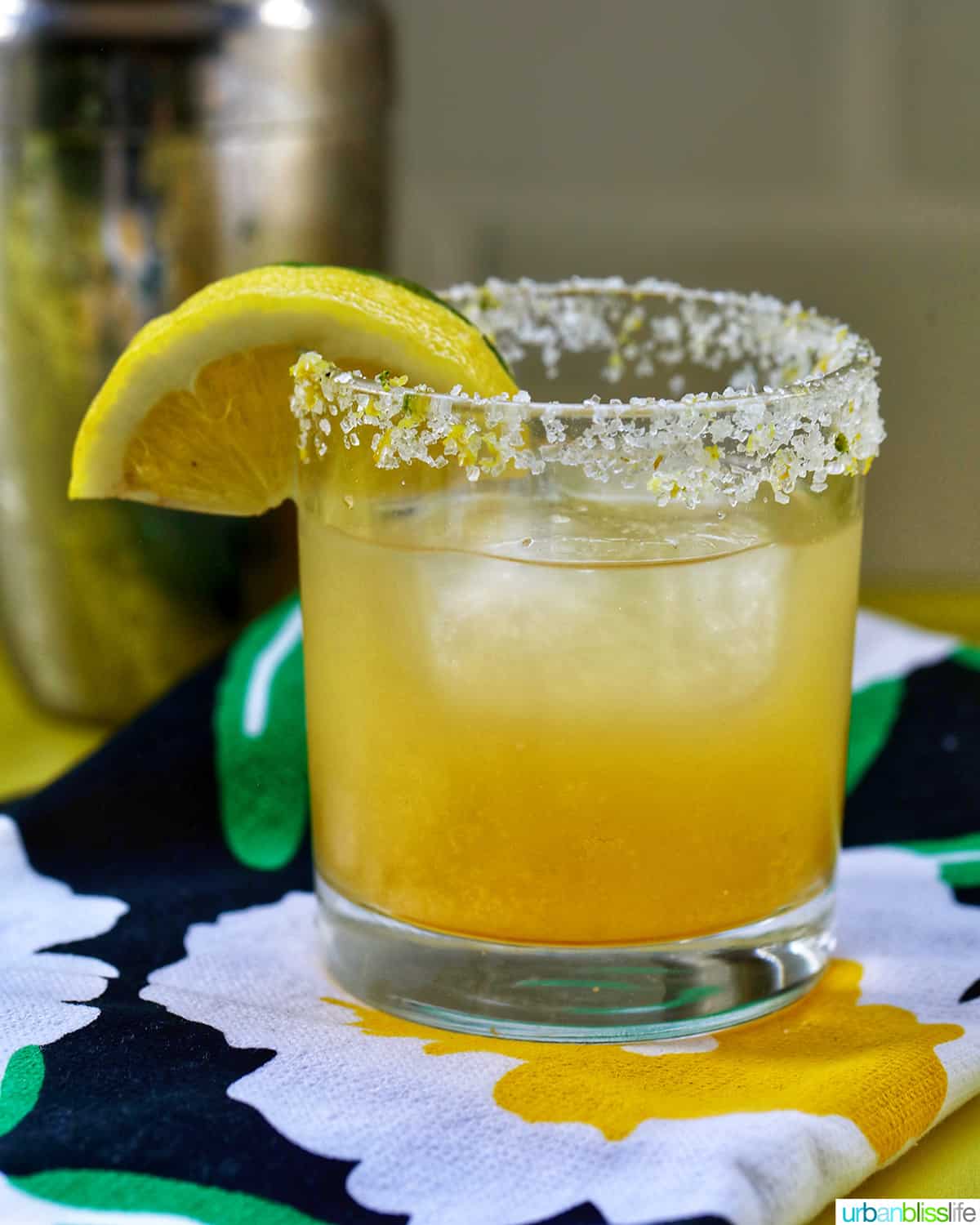 glass of yuzu margarita with slices of lemon and lime on brightly colored napkins.