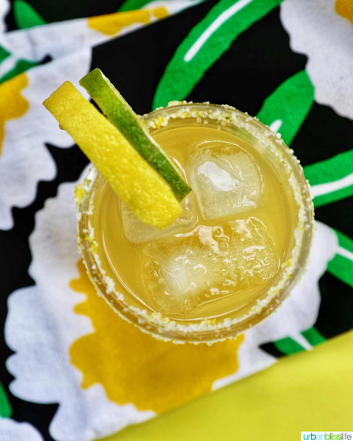 glass of yuzu margarita with slices of lemon and lime on brightly colored napkins.