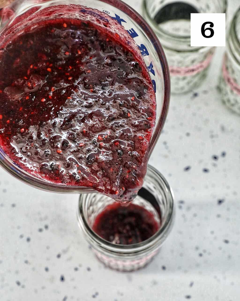 pouring blackberry freezer jam into a mason jar.