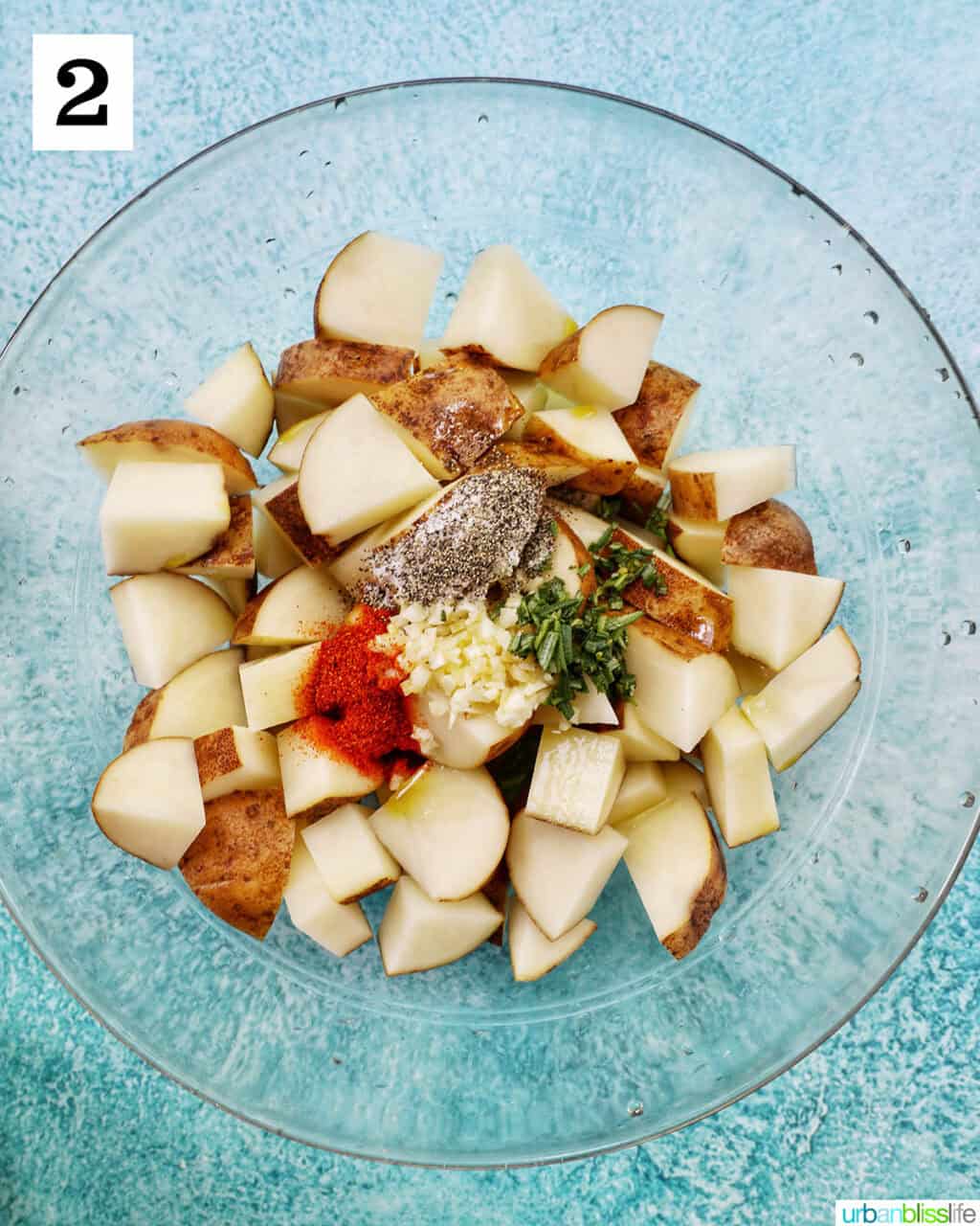 glass bowl with potato wedges, seasonings, and herbs.