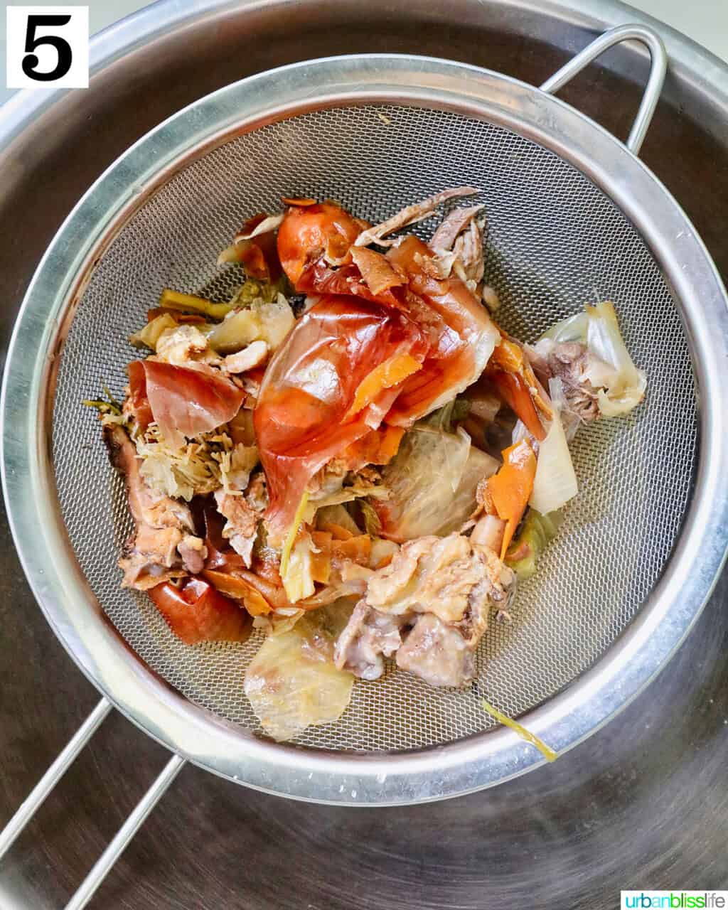 chicken bones and vegetable scraps strained over a bowl.