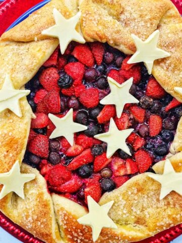 a mixed berry galette: mixed berries in pie dough with white chocolate stars on a red plate.