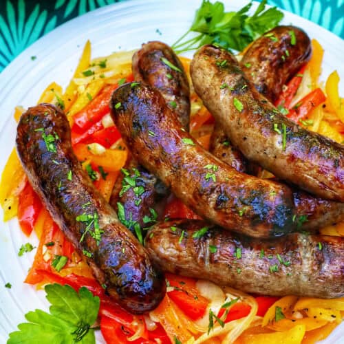 plate of grilled bratwurst over sauteed peppers.