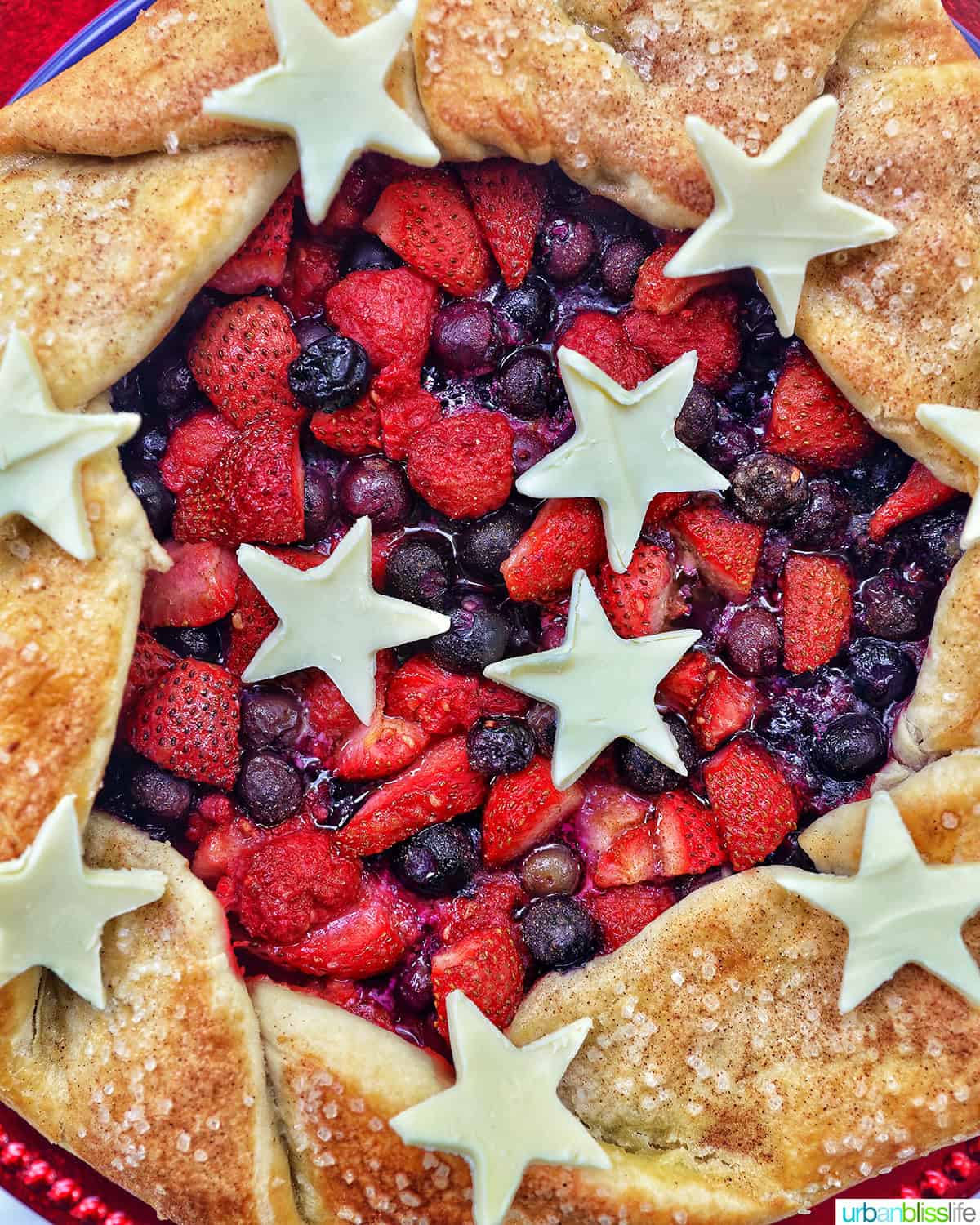 a mixed berry galette: mixed berries in pie dough with white chocolate stars on a red plate.