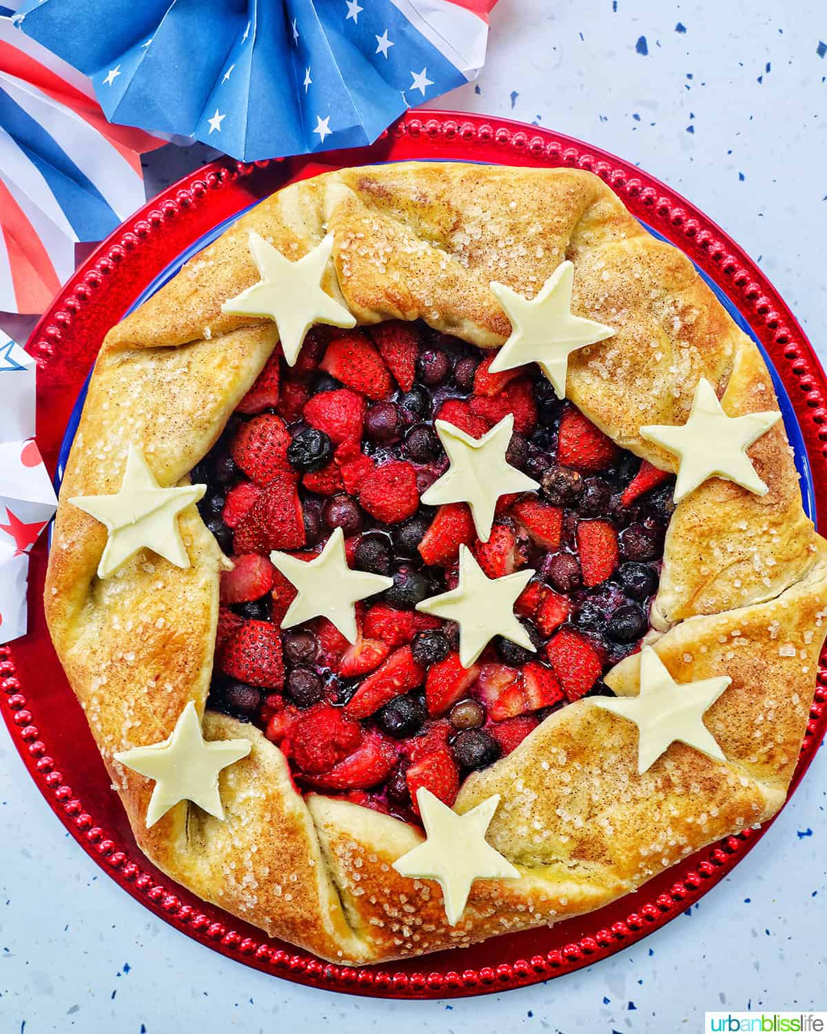 a mixed berry galette: mixed berries in pie dough with white chocolate stars on a red plate.