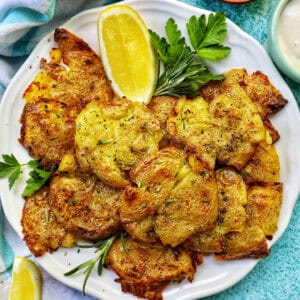 air fryer smashed potatoes on a plate with lemon wedges and herbs.