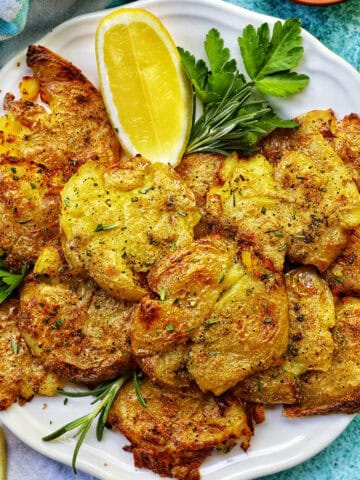 air fryer smashed potatoes on a plate with lemon wedges and herbs.