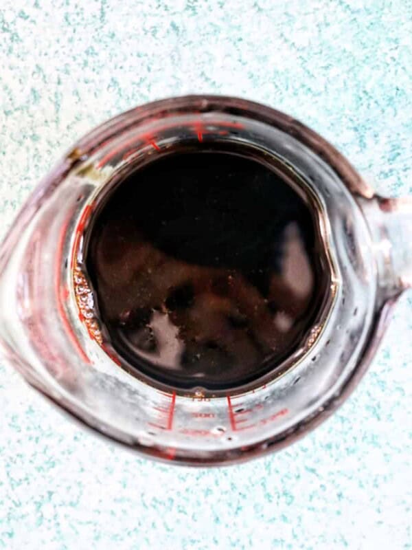 measuring cup of balsamic glaze on a blue background.