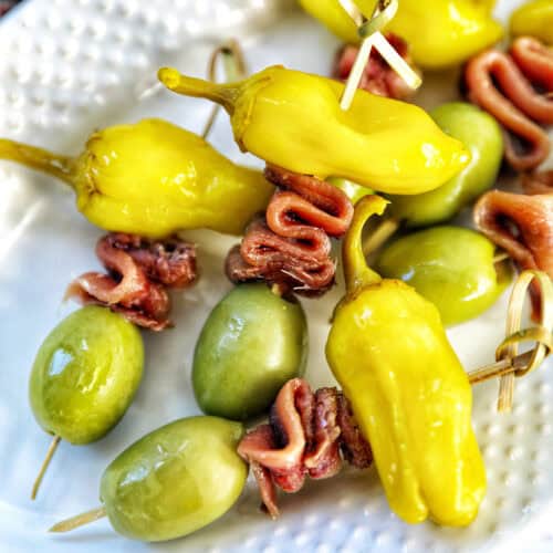 Gilda pintxos: food sticks with peppers, anchovies, and olives on a white plate.