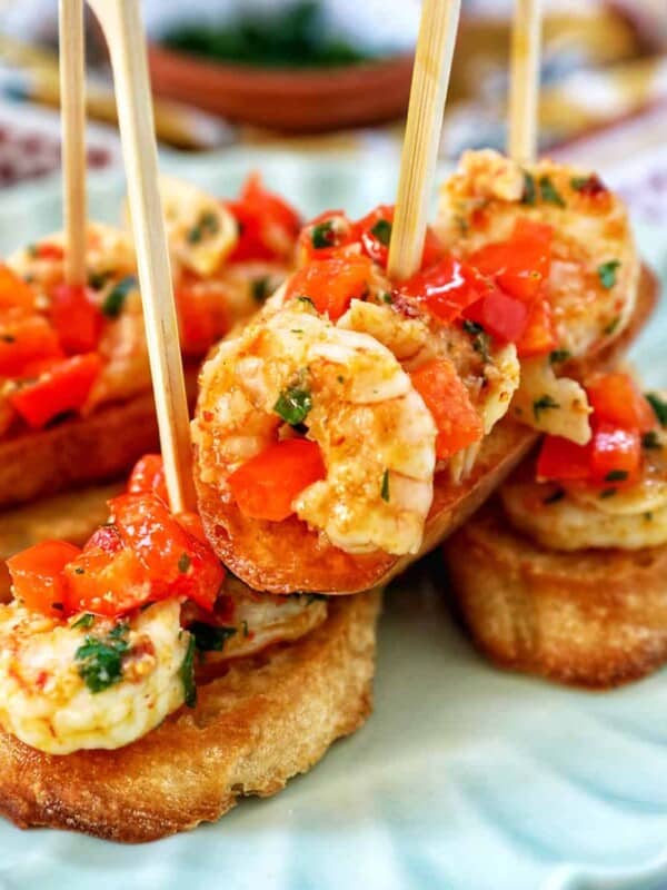 shrimp pintxos skewers with tomatoes on crostini bread on a scalloped plate.