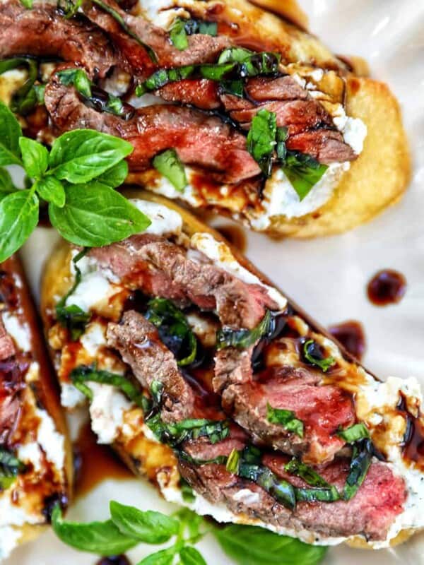 steak crostini with fresh basil leaves as garnish on a plate.
