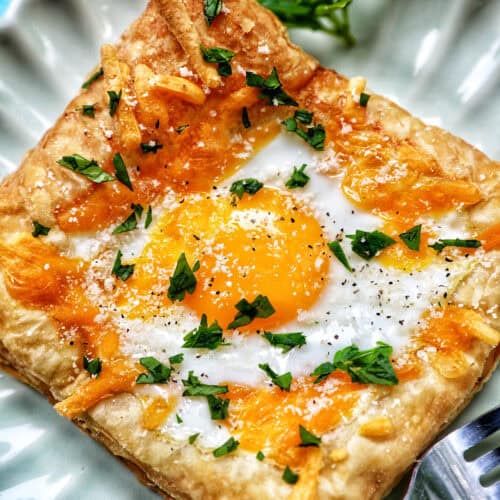 egg in puff pastry on a plate with parsley garnish.