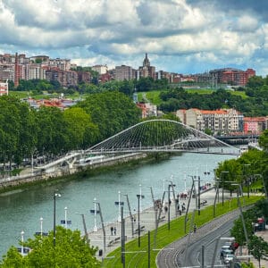 city view of Bilbao, Spain, a river, and white bridge.