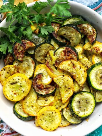 white bowl with air fryer zucchini and yellow squash and parsley garnish.