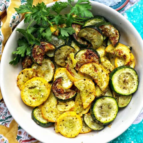 white bowl with air fryer zucchini and yellow squash and parsley garnish.