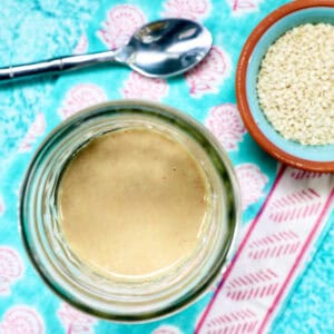 jar of homemade tahini with a small bowl of sesame seeds and a spoon.