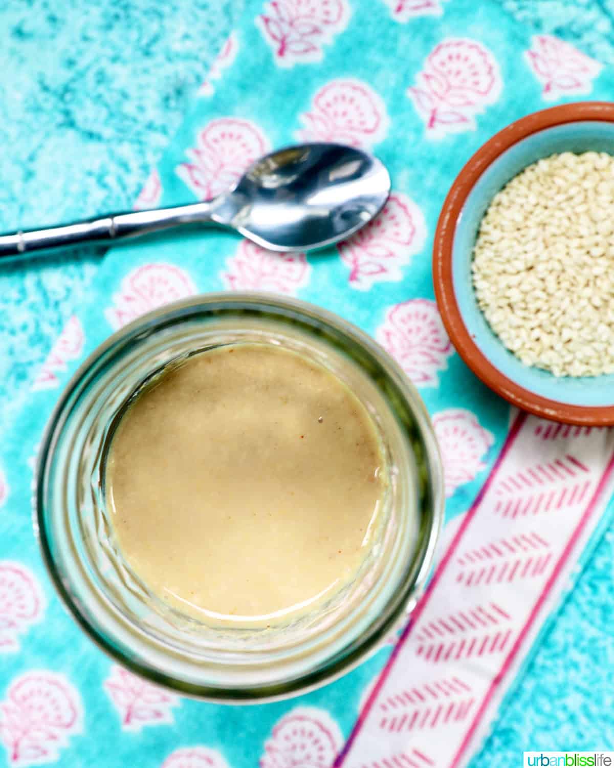 jar of homemade tahini with a small bowl of sesame seeds and a spoon.