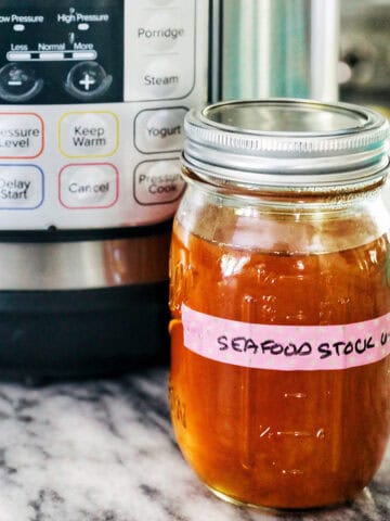 mason jar of seafood stock in front of an Instant Pot on marble.