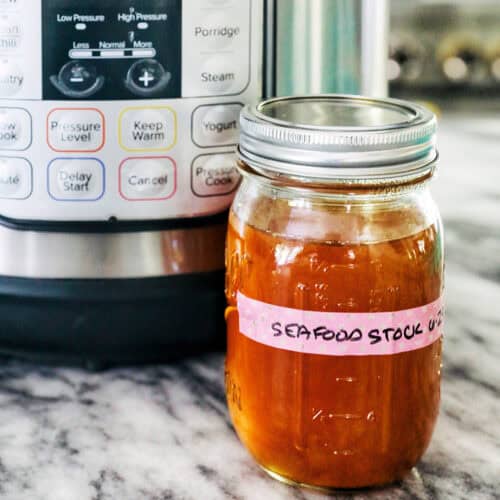 mason jar of seafood stock in front of an Instant Pot on marble.