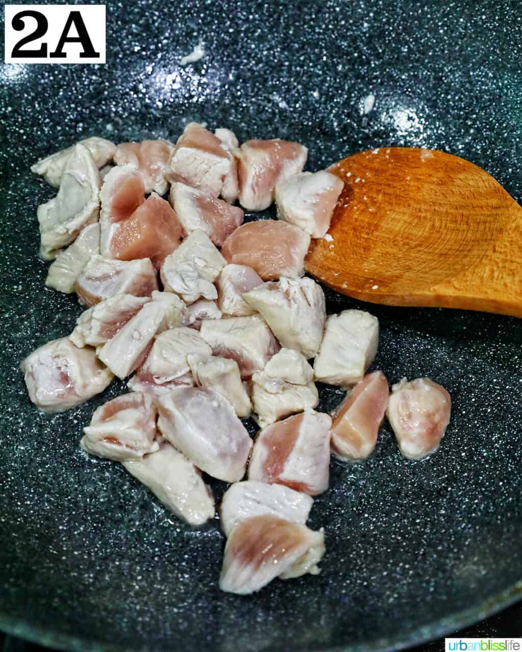 chicken pieces in a wok with a wooden spoon.