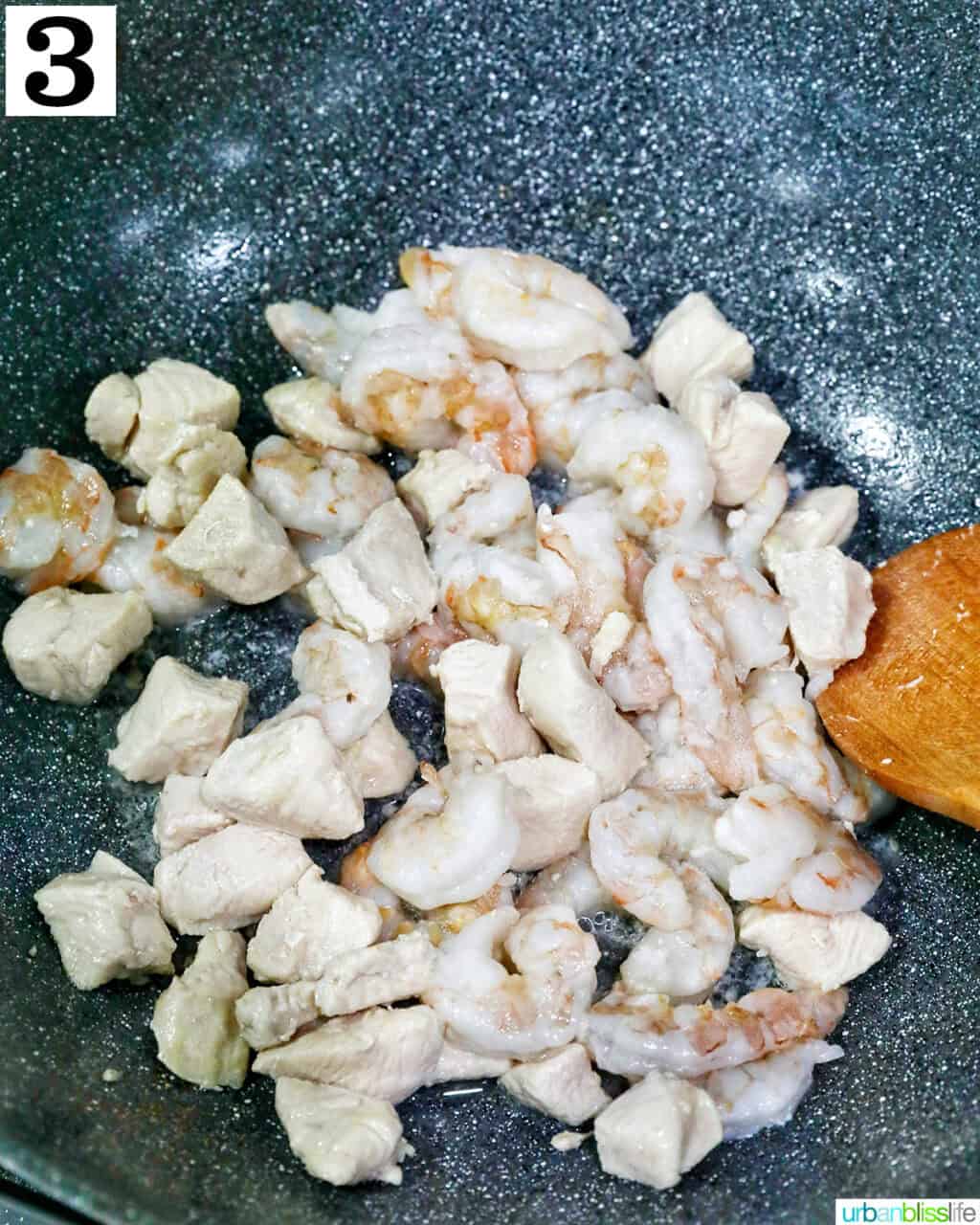 chicken pieces cooked in a wok with a wooden spoon.