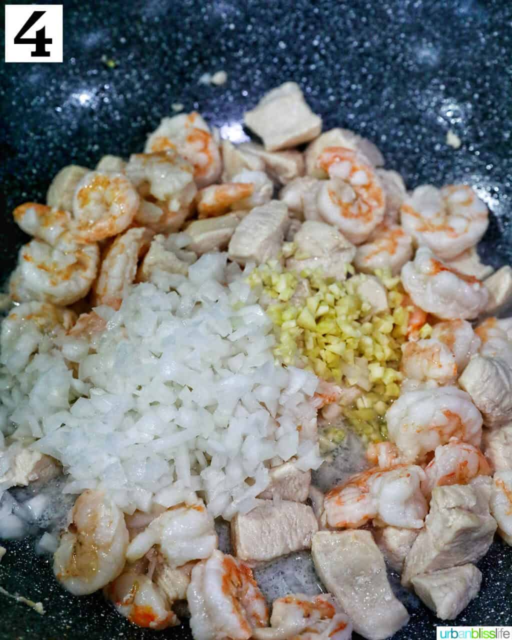 diced onions and minced garlic with chicken pieces in a wok.