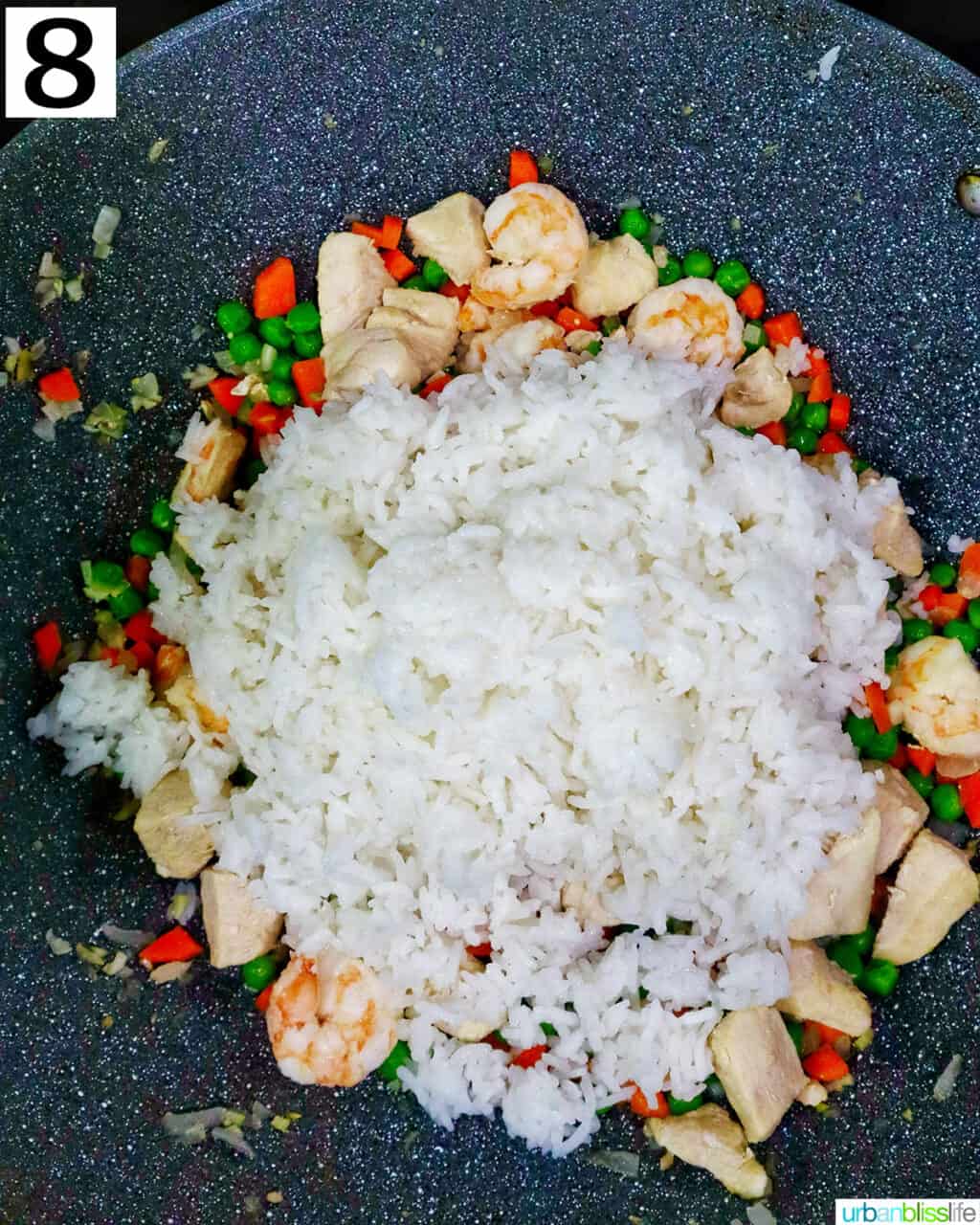 rice added to a wok with shrimp, chicken, and vegetables.         