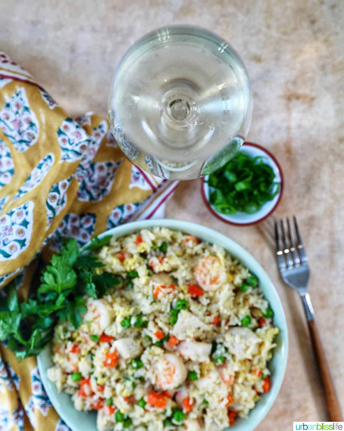 overhead of a glass of white wine and a bowl of shrimp and chicken fried rice. 