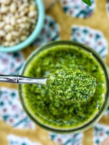 fresh basil pesto in a jar being spooned out of the jar.