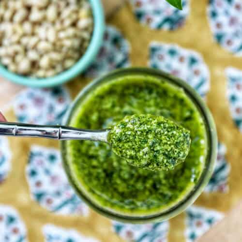 fresh basil pesto in a jar being spooned out of the jar.