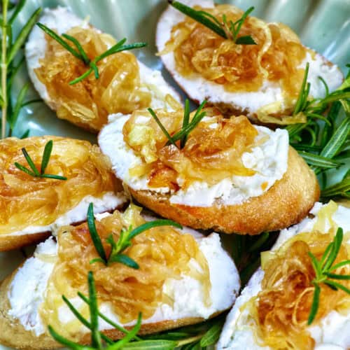 caramelized onions and goat cheese crostini on a plate with rosemary sprig garnish.