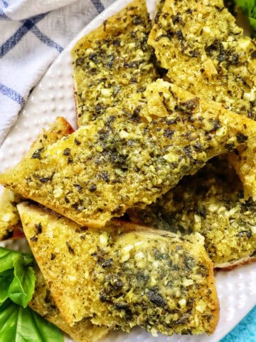 slices of pesto bread on a white platter with garnish of basil.