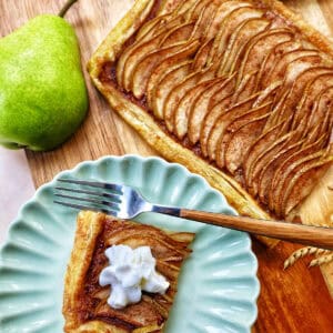 slice of pear tart on a plate with fork next to a full ginger and pear tart with puff pastry.