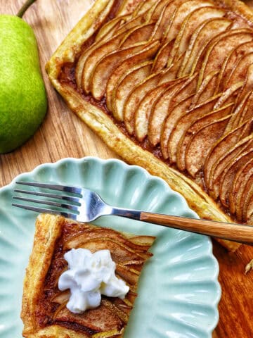 slice of pear tart on a plate with fork next to a full ginger and pear tart with puff pastry.