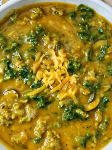 bowl of pumpkin soup with sausage, greens and cheese.