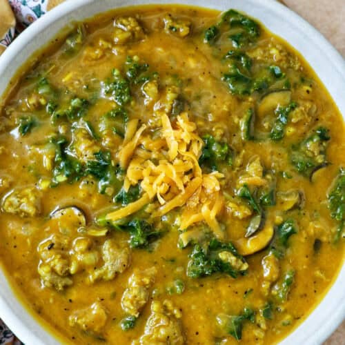 bowl of pumpkin soup with sausage, greens and cheese.