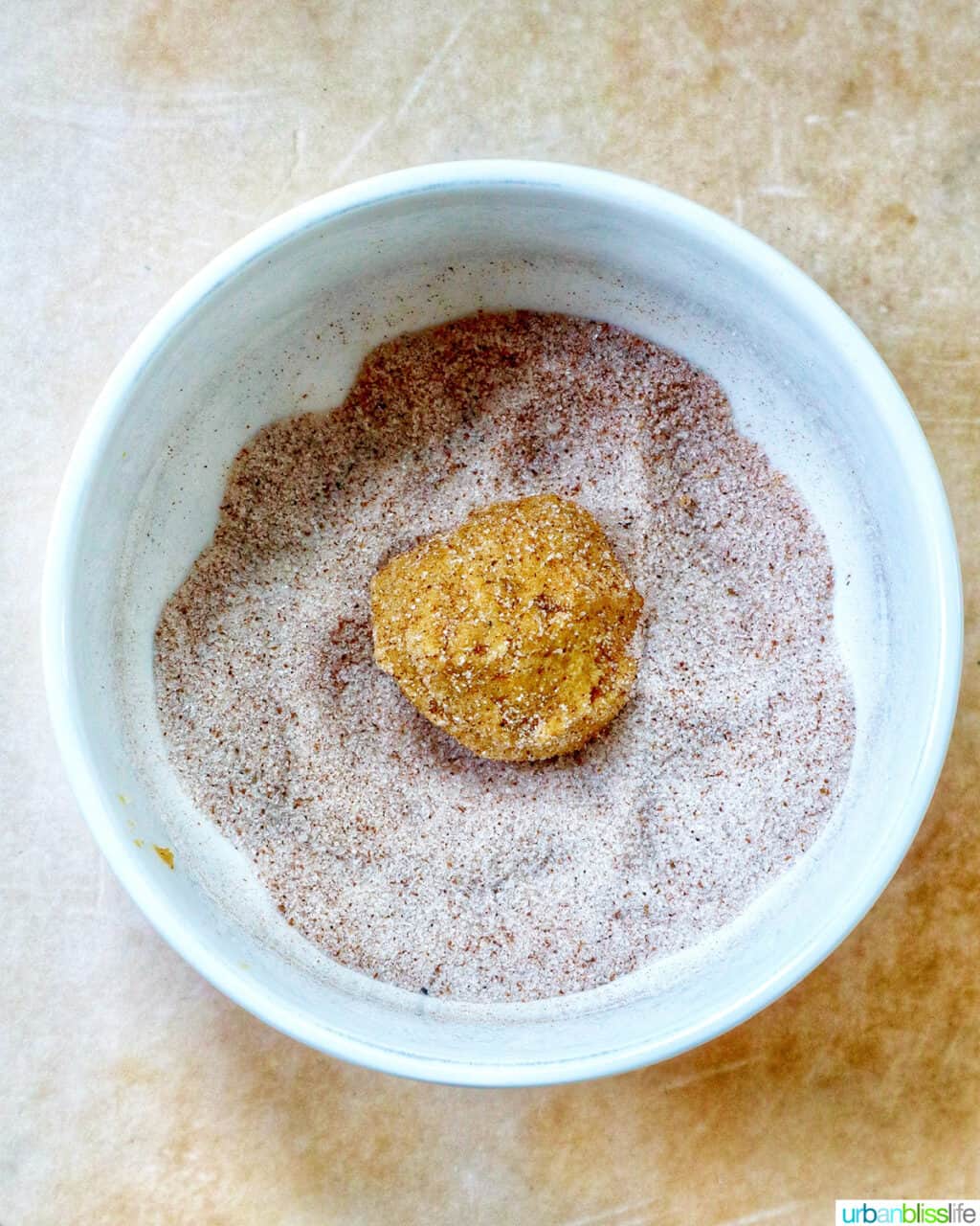 pumpkin pie spice cookie dough ball rolling in cinnamon sugar.