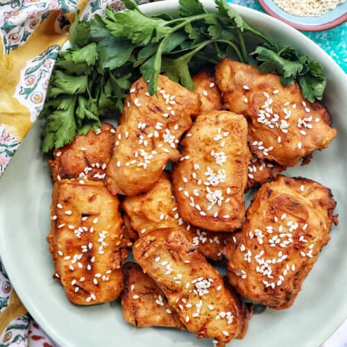 bowl of Thai fried bananas dessert with bowl of sesame seeds and herbs.