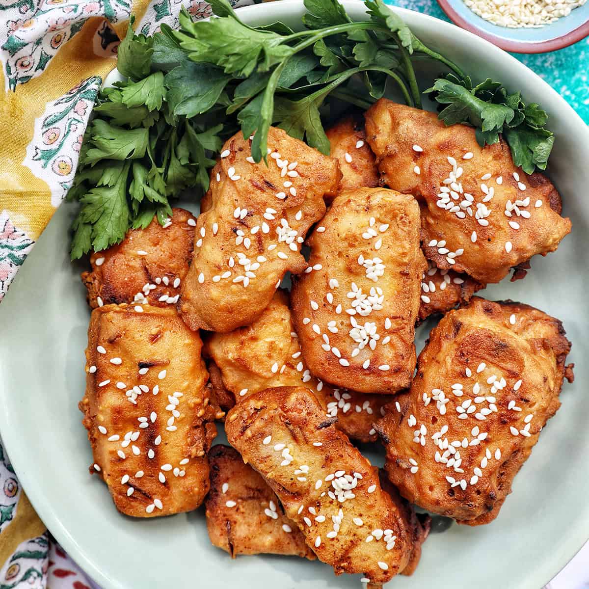 bowl of Thai fried bananas dessert with bowl of sesame seeds and herbs.