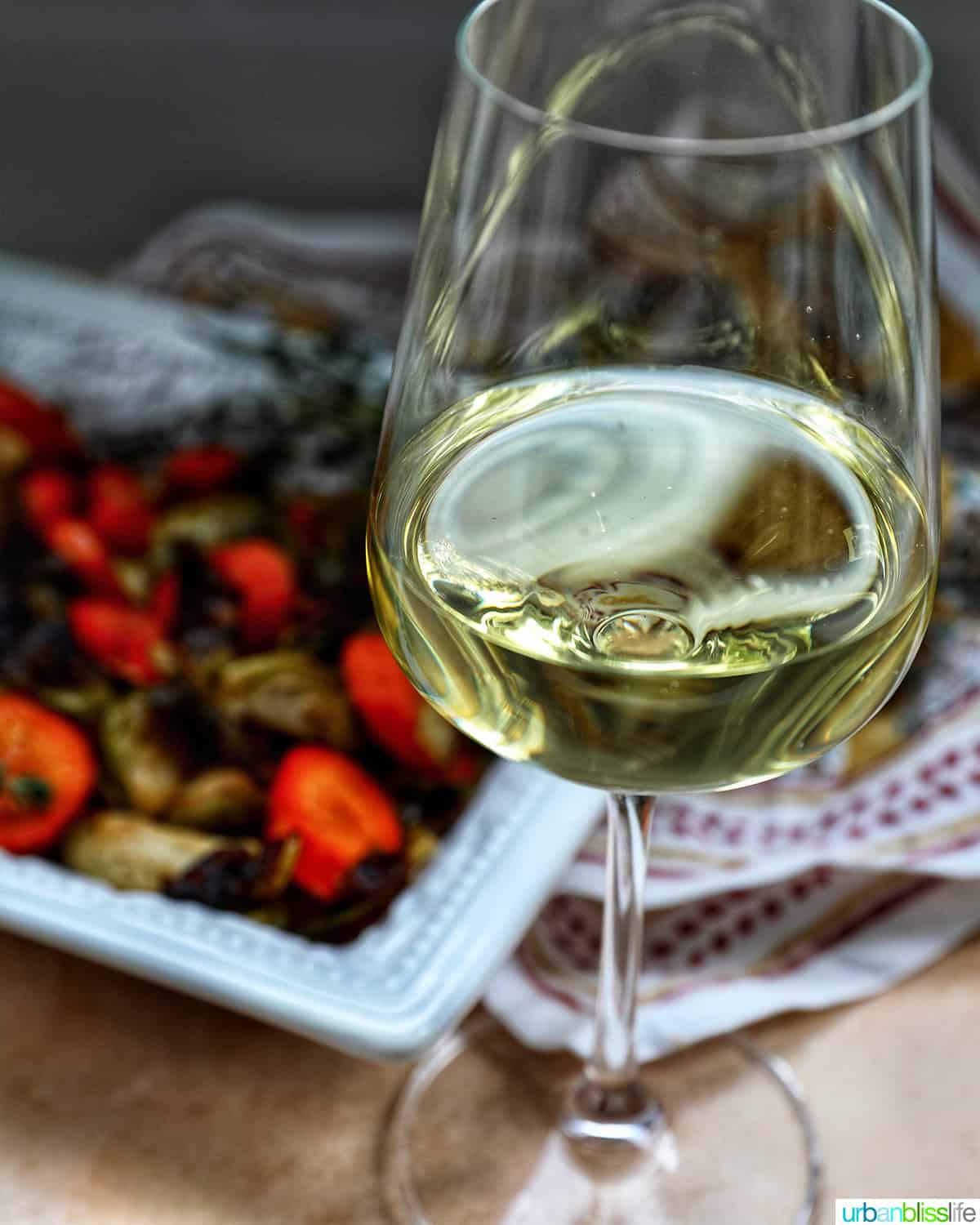 roasted brussels sprouts and carrot slices in a bowl with a glass of white wine.