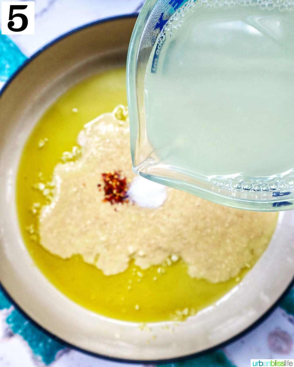 adding liquid to spices and garlic and olive oil in a saucepan.