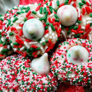 almond Christmas cookies with red and green sprinkles stacked on a plate.