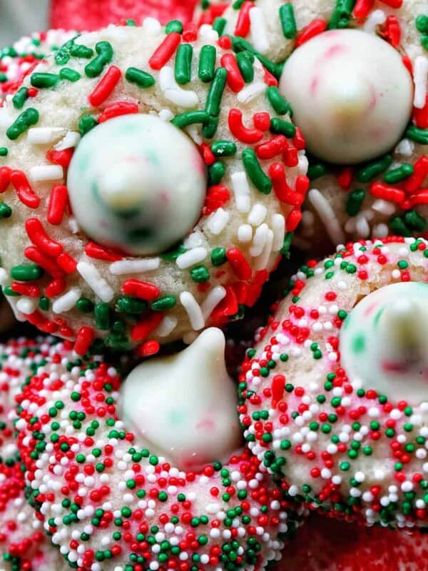 almond Christmas cookies with red and green sprinkles stacked on a plate.