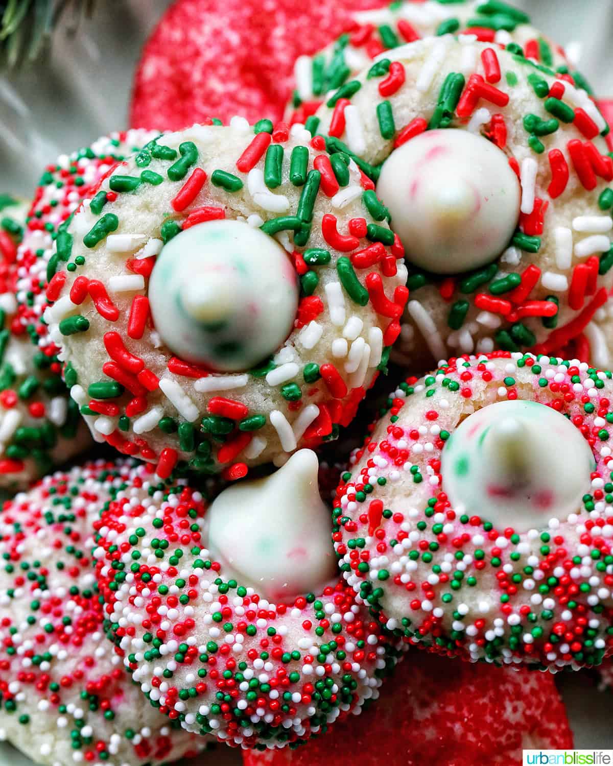 almond Christmas cookies with red and green sprinkles stacked on a plate.